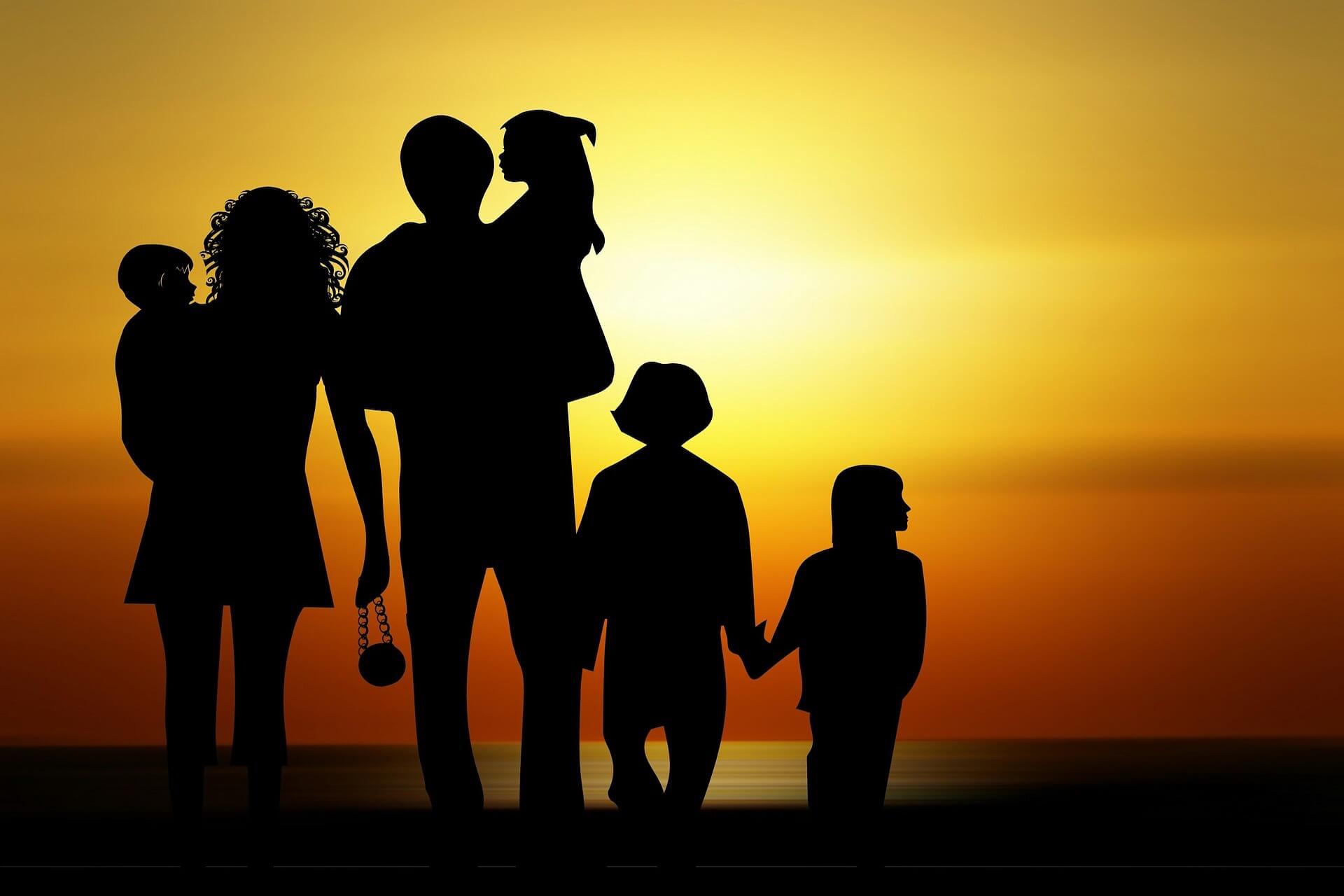 Silhouette of a mom, dad, and four kids standing in front of a sunset