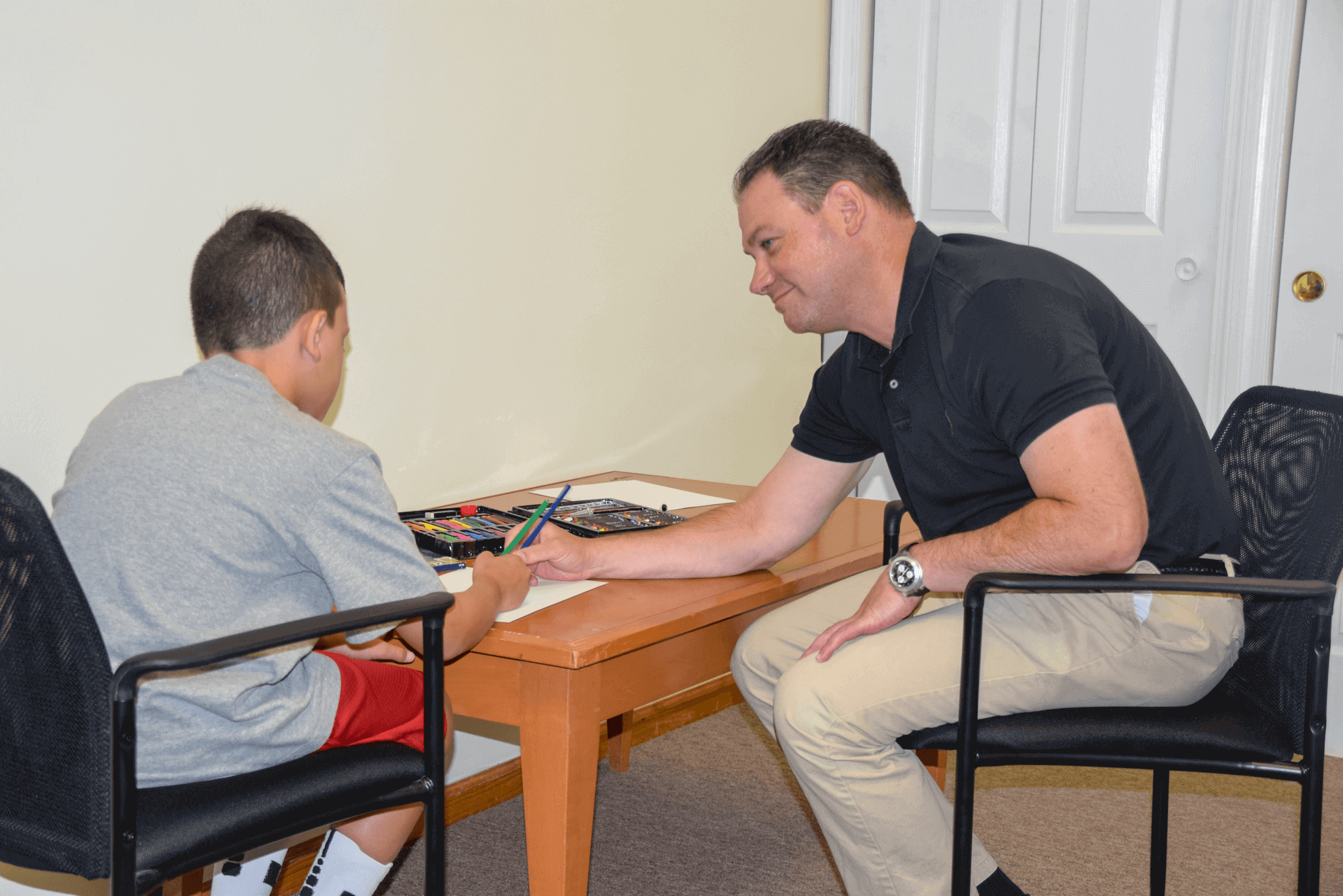 Joel Sperling and a young boy sitting around a table, drawing with colored pencils